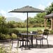 A black and white striped umbrella over a black table and chairs on a patio.