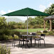 A table and chairs under a Lancaster Table & Seating forest green umbrella on a patio.