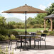 A table and chairs under a Lancaster Table & Seating black umbrella on a patio.