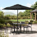 A table with chairs under a black Lancaster Table & Seating umbrella on a stone patio.