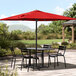 A Lancaster Table & Seating black table and chairs under a red umbrella on a patio.