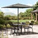 A black and white striped Lancaster Table & Seating umbrella over a table with chairs on an outdoor patio.