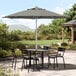 A Lancaster Table & Seating black and white striped umbrella over a table and chairs on an outdoor patio.