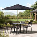 A table and chairs under a navy Lancaster Table & Seating umbrella on a patio.