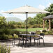 A white Lancaster Table & Seating umbrella over a table and chairs on an outdoor patio.