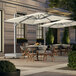 A Lancaster Table & Seating ivory cantilever umbrella with lights over a table on an outdoor patio.