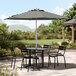 A table with black and white striped umbrella shading black chairs.