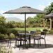 A Lancaster Table & Seating black metal table and chairs under a round black umbrella on a patio.