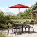 A red Lancaster Table & Seating umbrella on a table with chairs on a stone patio.