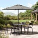 A table with black chairs under a Lancaster Table & Seating black and white striped umbrella on an outdoor patio.