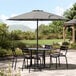 A Lancaster Table & Seating pewter gray umbrella on a table with chairs on a patio.