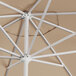 A close-up of a tan Lancaster Table & Seating aluminum umbrella with white poles.