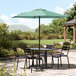 A black Lancaster Table & Seating umbrella on a patio table with chairs.