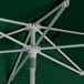 A Lancaster Table & Seating forest green umbrella with a white metal pole.