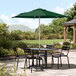 A forest green Lancaster Table & Seating umbrella over a table with chairs on an outdoor patio.