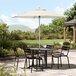 A Lancaster Table & Seating ivory umbrella over a table and chairs on a patio.