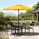 A Lancaster Table & Seating yellow umbrella on a patio table with chairs.