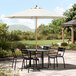 A white Lancaster Table & Seating umbrella shading a table and chairs on an outdoor patio.