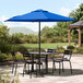 A black table and chairs under a blue Lancaster Table & Seating umbrella on a patio.