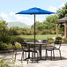 A black table and chairs on a stone patio with a Lancaster Table & Seating blue umbrella.