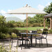 A white Lancaster Table & Seating umbrella over a table with chairs on a stone patio.