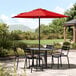 A table and chairs on a patio with a red umbrella.