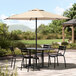 A black metal table and chairs under a black Lancaster Table & Seating umbrella on a brick patio.