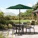 A Lancaster Table & Seating forest green umbrella over a table with chairs on a stone patio.