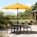 A yellow Lancaster Table & Seating umbrella on a black table on a patio.