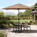 A table and chairs under a Lancaster Table & Seating black umbrella on a patio.