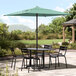 A black Lancaster Table & Seating umbrella shading a table with chairs on an outdoor patio.