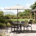 A round white table with chairs and a black steel umbrella on a stone patio.