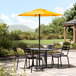 A Lancaster Table & Seating yellow umbrella over a table with chairs on a patio.