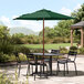 A Lancaster Table & Seating forest green umbrella over a table with chairs on a stone patio.