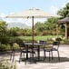 A Lancaster Table & Seating ivory umbrella over a table with chairs on a patio.