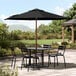 A Lancaster Table & Seating black woodgrain umbrella shading a table and chairs on a stone patio.