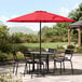 A table and chairs under a red Lancaster Table & Seating umbrella on a stone patio.