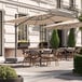 A patio with tables and chairs under a Lancaster Table & Seating aluminum cantilever umbrella.