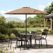 A table and chairs under a Lancaster Table & Seating mocha umbrella on a stone patio.