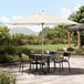 A table and chairs under a Lancaster Table & Seating ivory umbrella on a patio.