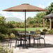 A table and chairs under a Lancaster Table & Seating black steel umbrella on a stone patio.