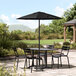 A black Lancaster Table & Seating umbrella on a patio table with chairs.