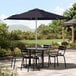 A Lancaster Table & Seating round table and chairs under a navy umbrella on a patio.