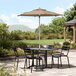 A Lancaster Table & Seating round table with chairs and a wheat umbrella on an outdoor patio.