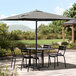 A Lancaster Table & Seating black aluminum table with an umbrella over chairs.