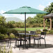 A black Lancaster Table & Seating umbrella shading a table and chairs on an outdoor patio.