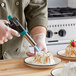 A person using a Choice butane torch to brown a dessert on a plate.