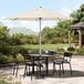 A table and chairs under a Lancaster Table & Seating ivory umbrella on a patio.