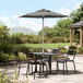 A black and white striped umbrella on a table with black chairs on a stone patio.