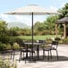 A Lancaster Table & Seating white umbrella over a table and chairs on a stone patio.